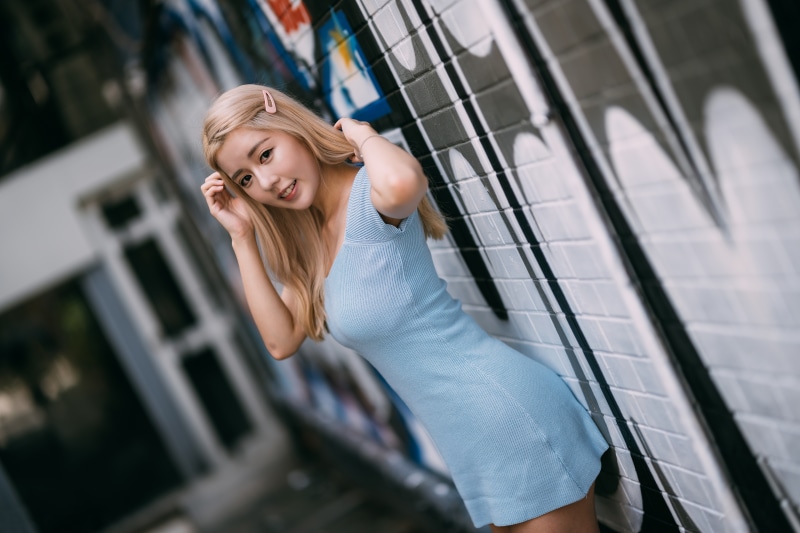 Blonde Asian girl in blue dress posing by graffiti wall
