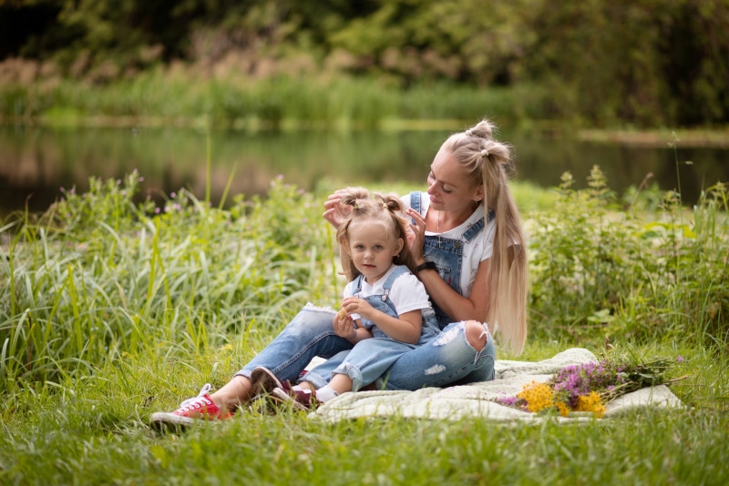 Mother combing daughter's hair by the lake