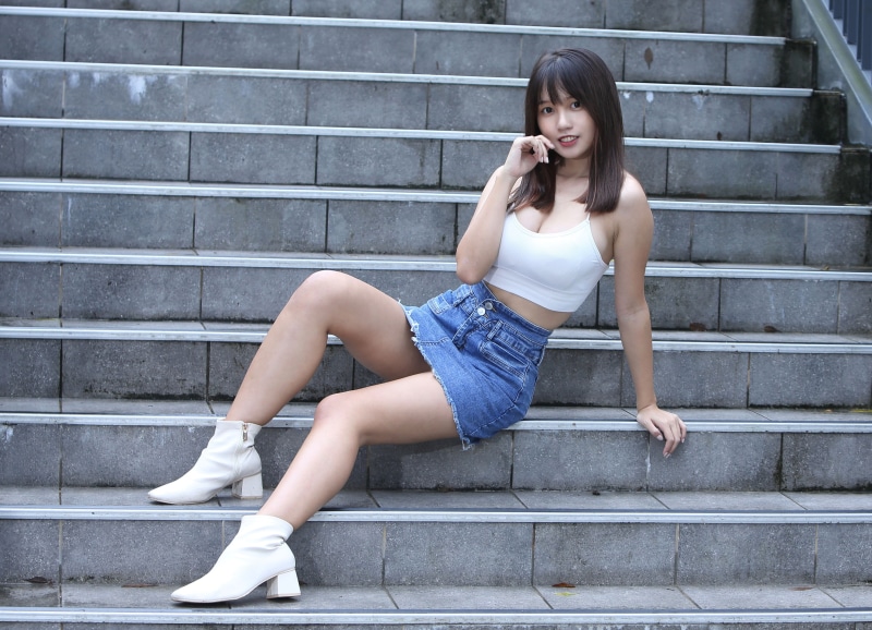Asian woman sitting on stairs wearing a white singlet and denim skirt