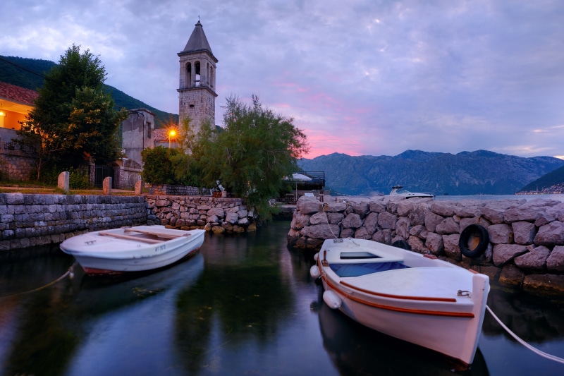 Boats by a waterfront tower in Stoliv, Montenegro at dusk