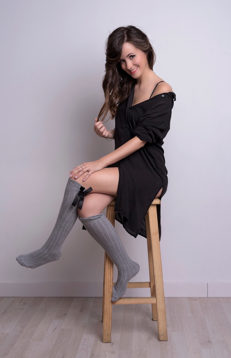 Woman in black dress and knee-high socks sitting on stool