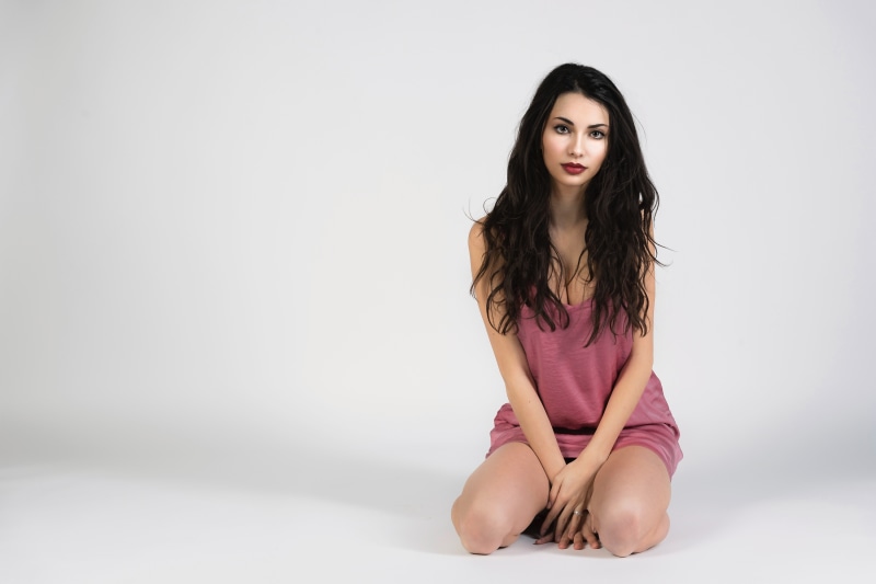 Brunette woman in pink dress kneeling on gray background