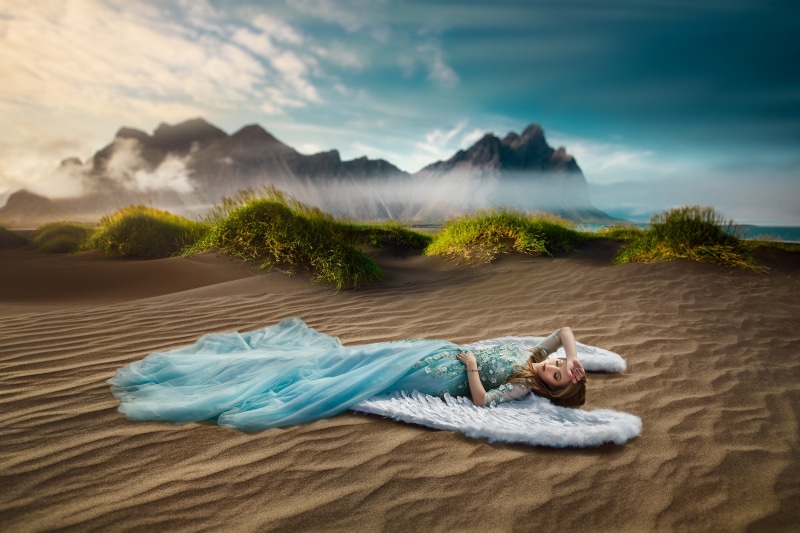 Woman in blue dress lying on angel wings in sand dunes