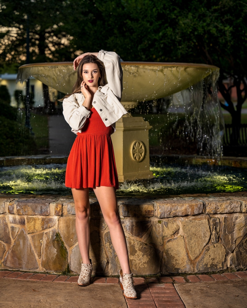 Ashley in a red dress and jacket posing by a fountain