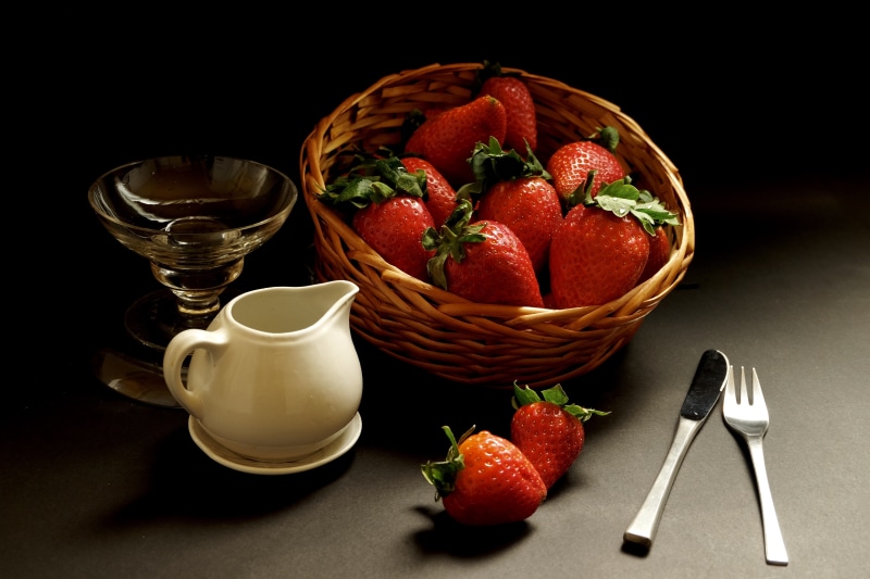 Strawberries in a wicker basket with a pitcher and cutlery