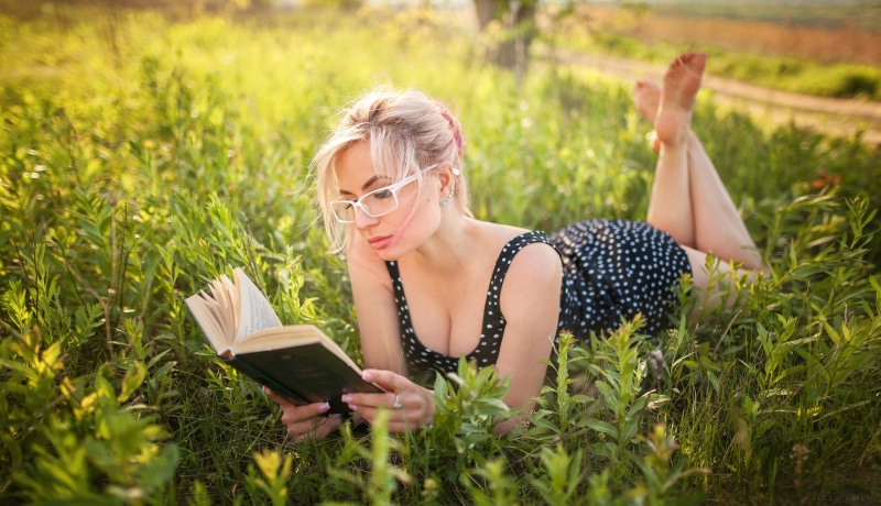 Blonde woman in polka dot dress reading a book in grass