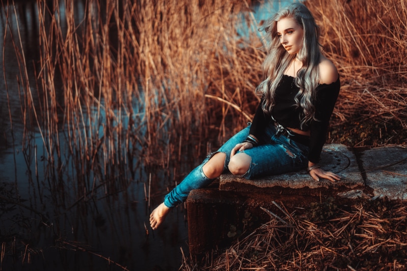 Woman in ripped jeans sitting by reeds