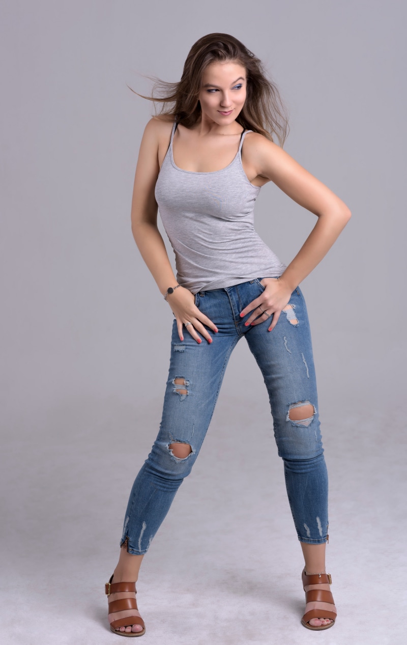 Woman in gray singlet and ripped jeans posing