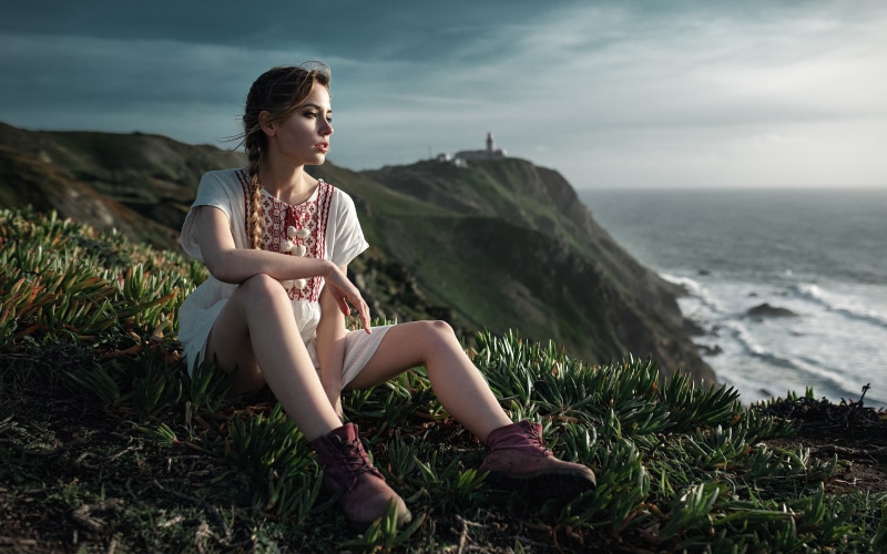 Woman with braid sitting on a cliff overlooking the ocean