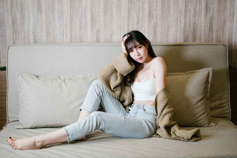 Asian woman in jeans and singlet sitting on couch