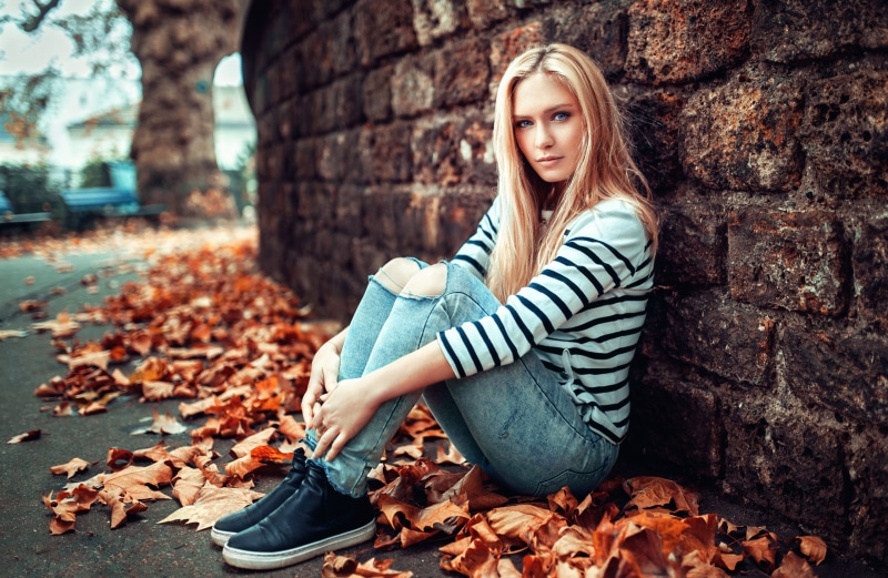 Blonde girl sitting by a brick wall in autumn