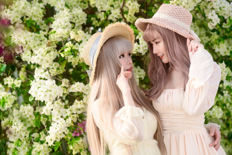 Two Asian women with dark blonde hair wearing hats and dresses