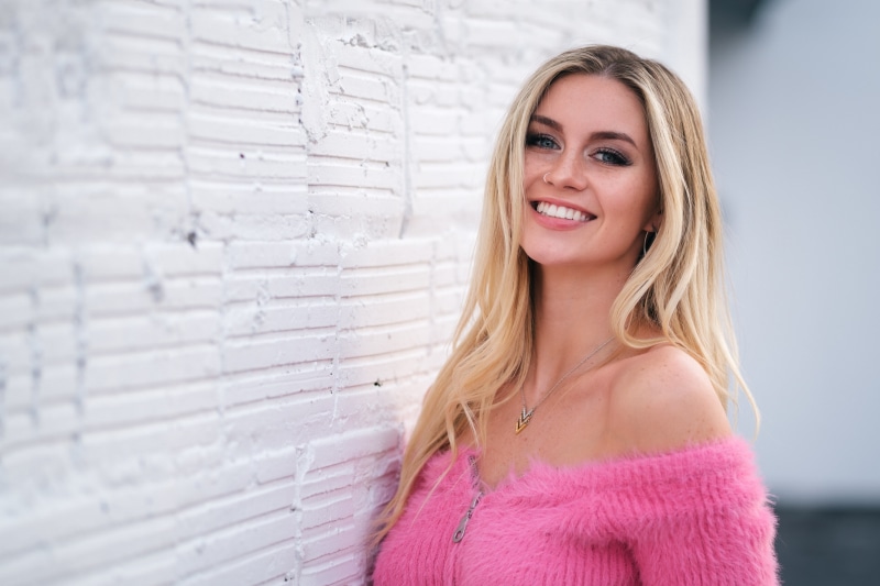 Blonde girl smiling by a white brick wall