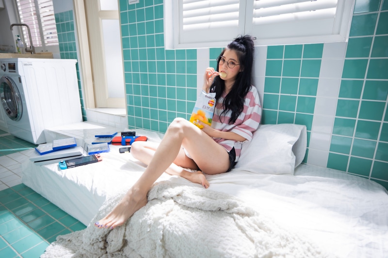 Asian girl with glasses eating chips on bed
