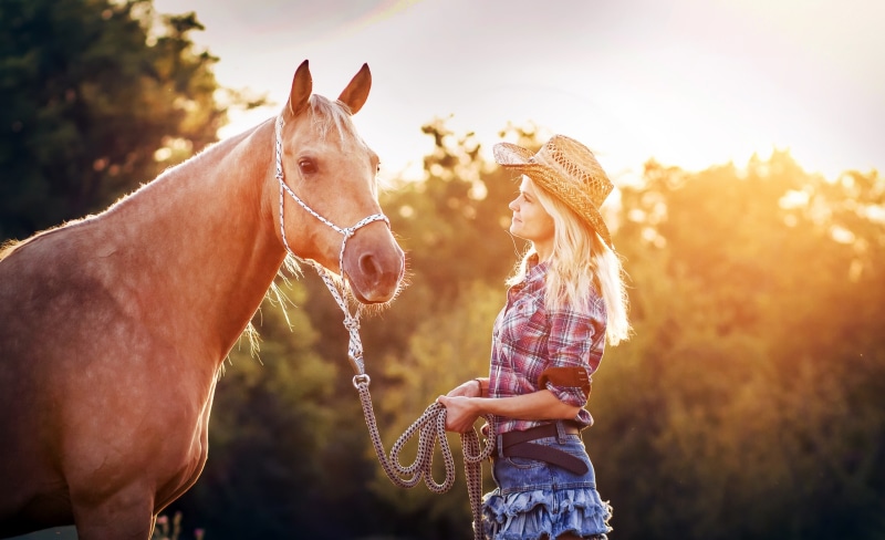 Blonde woman in cowboy hat with horse at sunset
