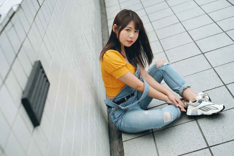 Asian woman sitting on tiled floor wearing overalls