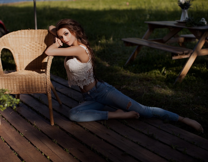 Woman in jeans and white top posing by armchair