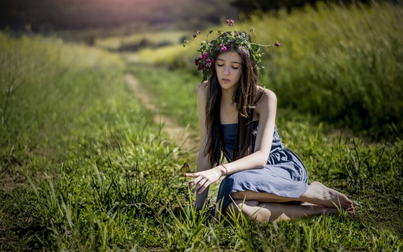 Girl with flower wreath and butterfly in grass