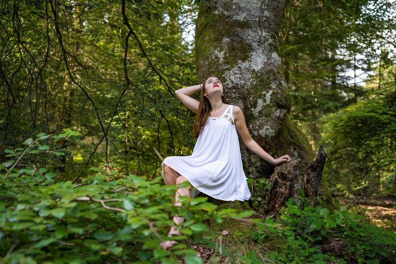Woman in white dress sitting by a tree in a forest