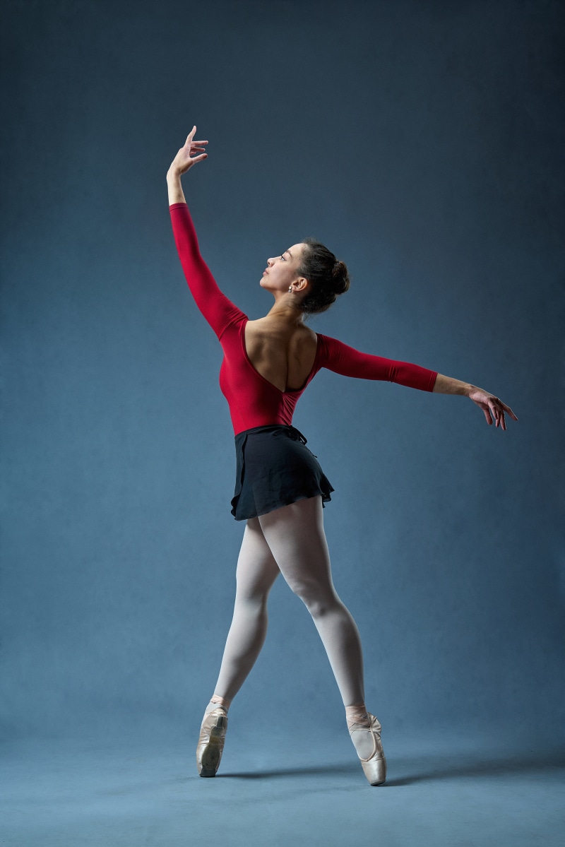 Ballerina in red leotard and black skirt on blue background
