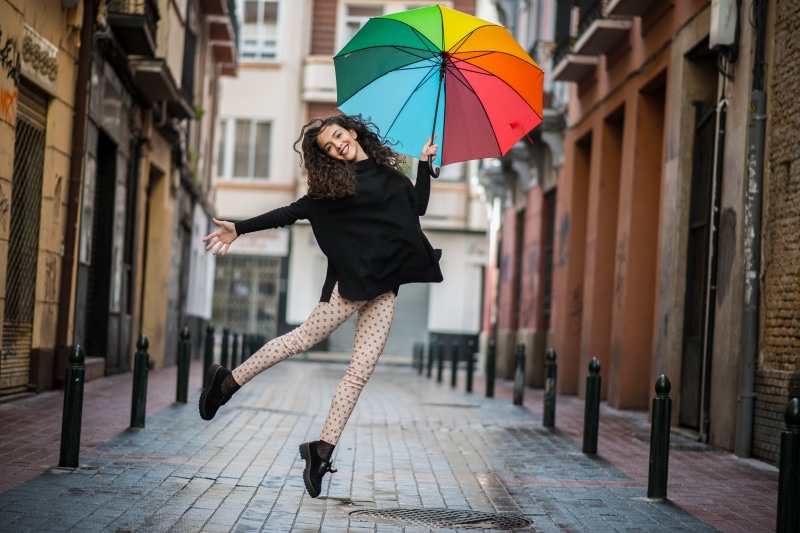 Yassmina jumping with a rainbow umbrella