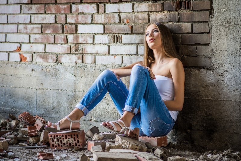 Woman in jeans sitting by a brick wall