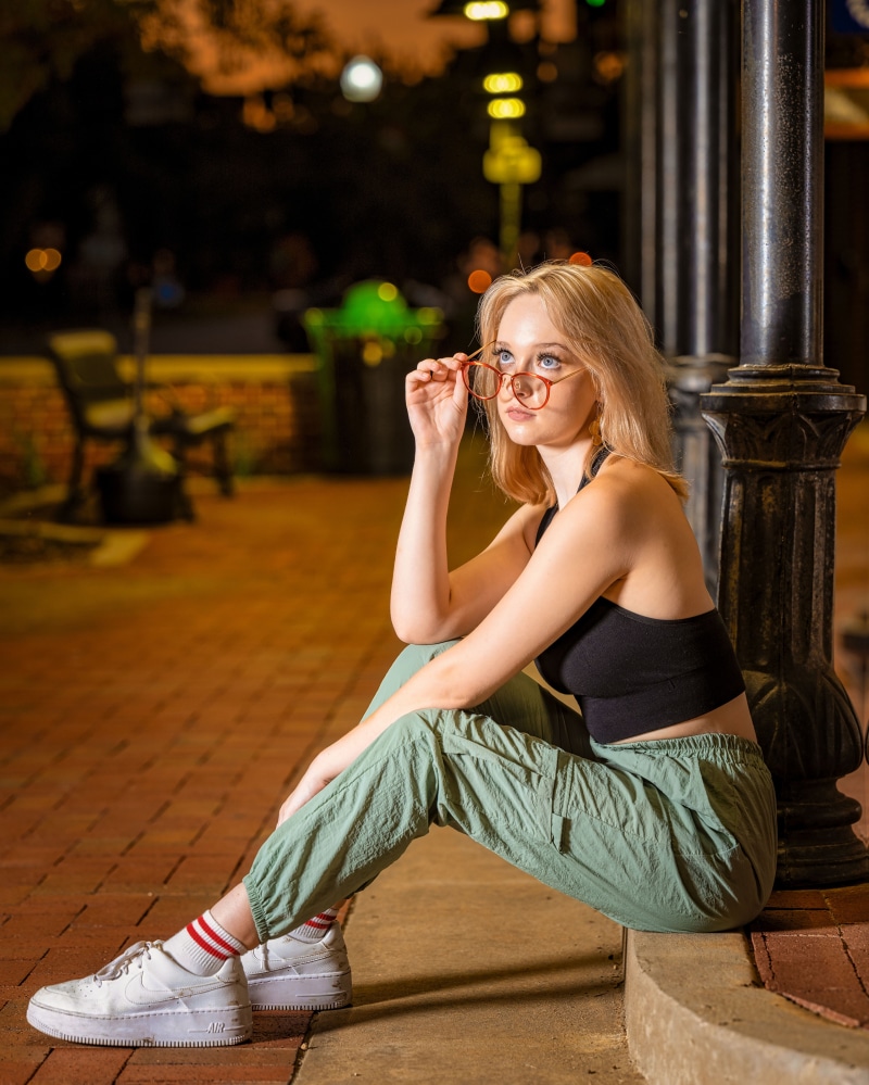 Blonde girl wearing glasses sitting by a lamppost
