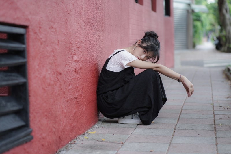 Asian girl in black overalls posing by red wall