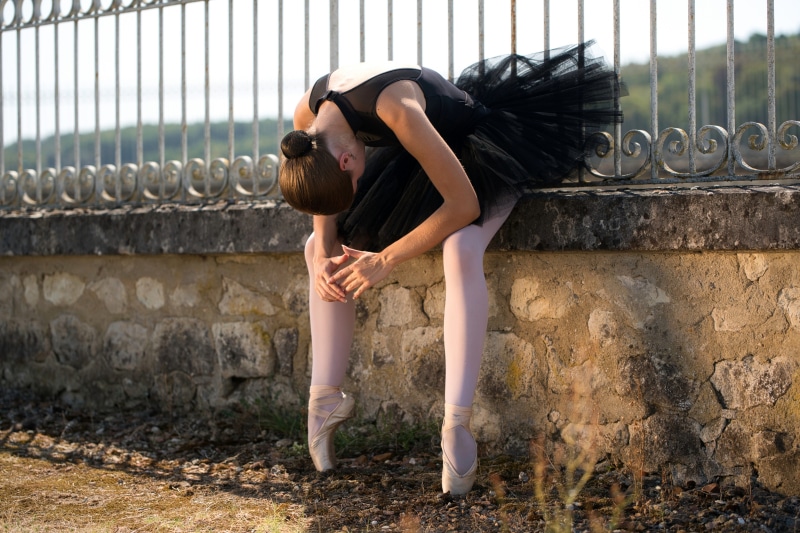 Ballerina in black tutu sitting on a stone fence