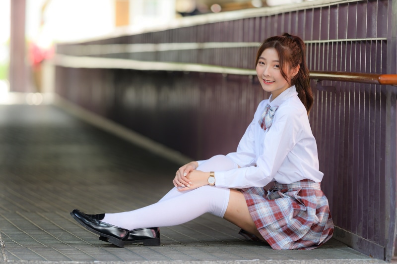 Asian schoolgirl in uniform sitting on a walkway