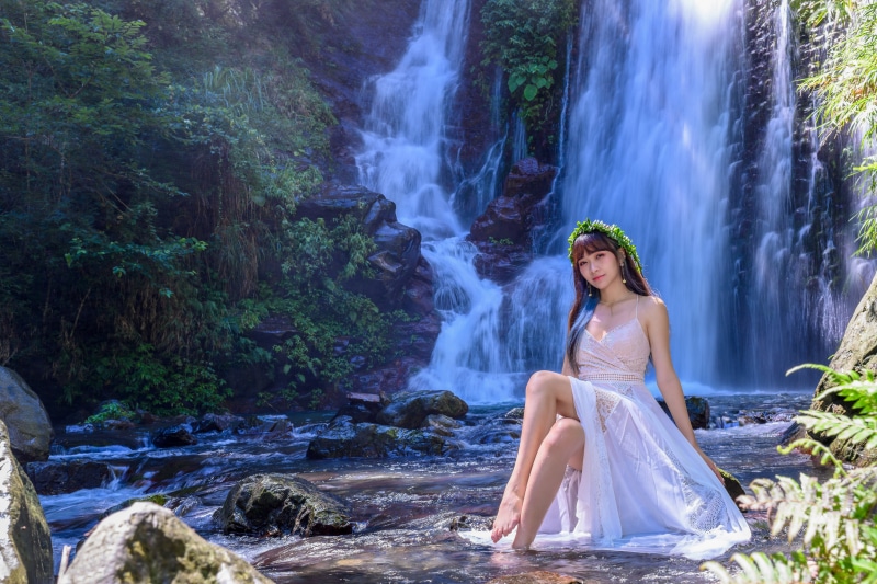 Asian woman with wreath sitting by waterfall