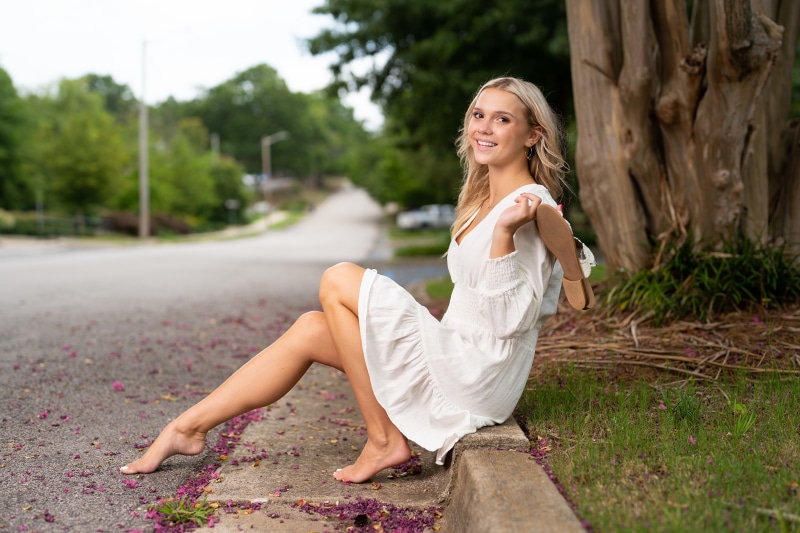 Blonde girl in white dress sitting on curb