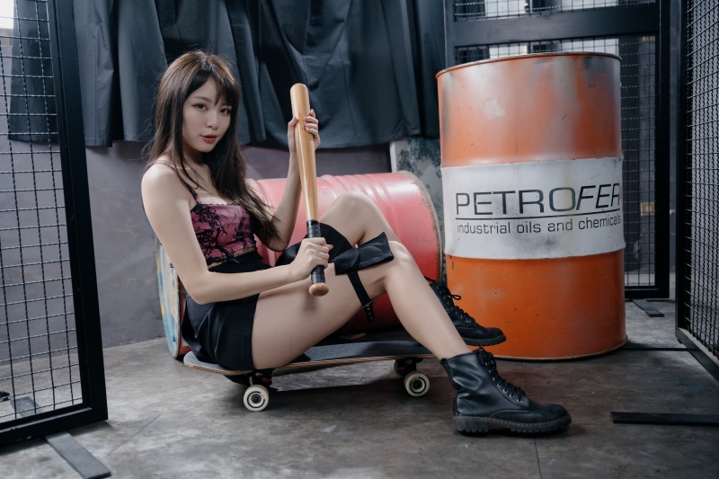 Asian girl with baseball bat on skateboard near barrels