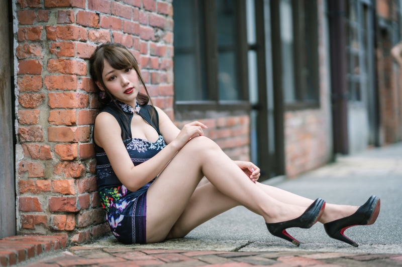 Asian woman in dress sitting by brick wall