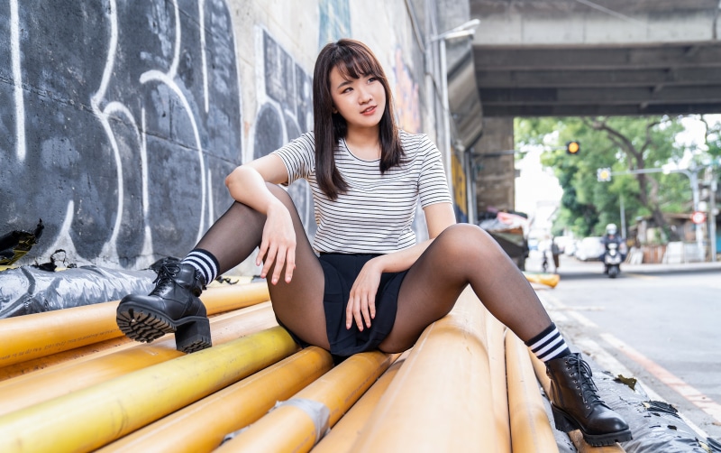 Asian girl sitting on pipes wearing boots and pantyhose
