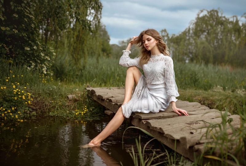 Woman in white dress sitting on a wooden bridge over water