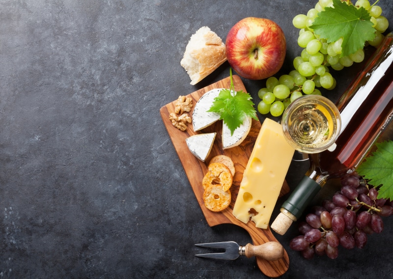 Cheese, Grapes, Apple, Wine, and Bread on Cutting Board
