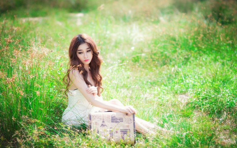 Asian woman with suitcase sitting in grass