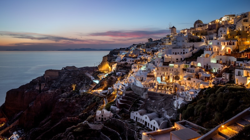 Oia, Greece at dusk with illuminated houses on a cliffside