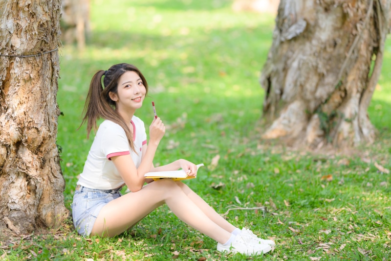 Asian woman sitting in grass with book and pen