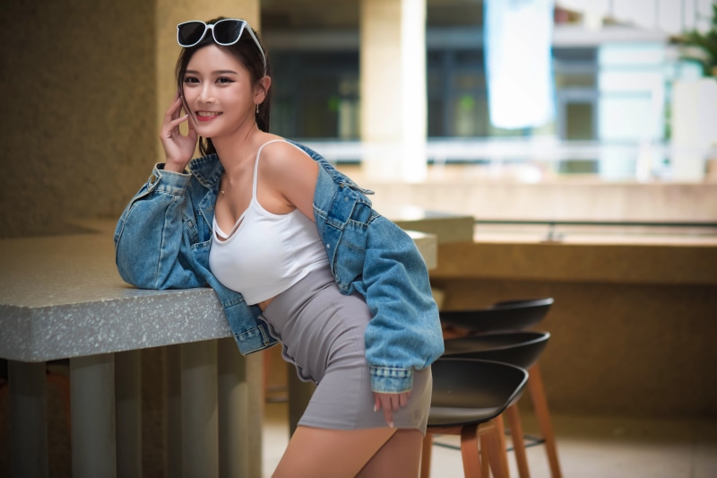 Asian woman wearing sunglasses, denim jacket, and skirt