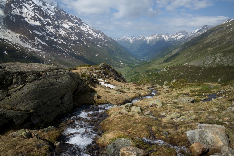 Stream flowing through rocky alpine valley with snow-capped mountains