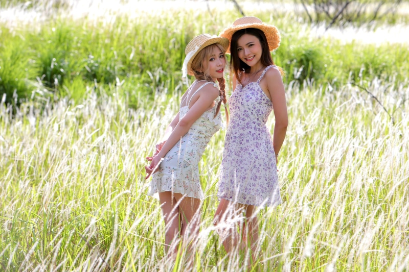 Two Asian women in dresses and hats in a field