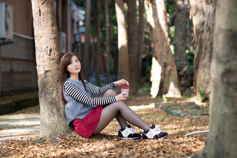 Asian woman with brown hair sitting by a tree with coffee