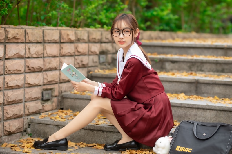 Girl in school uniform reading a book on stairs