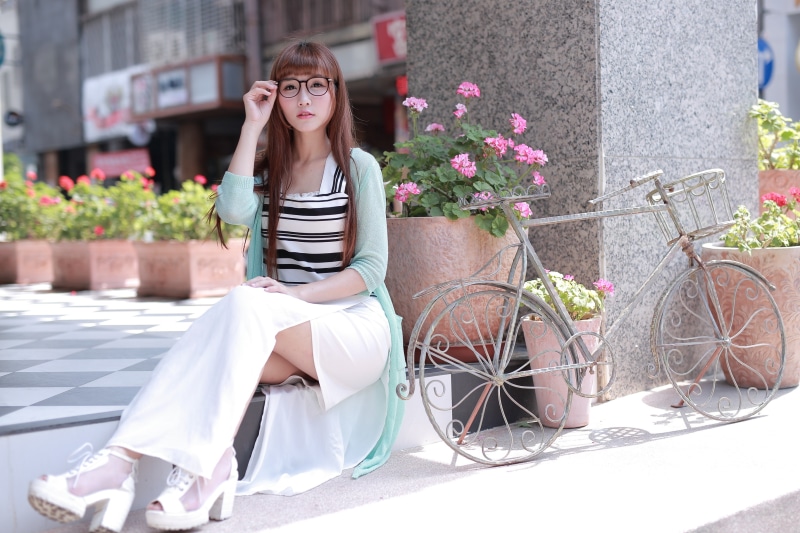 Asian woman with glasses sitting by a bicycle and flowers