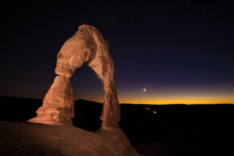 Delicate Arch at night with crescent moon and stars