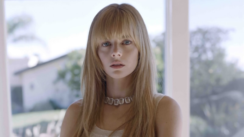 Model with blonde hair and bangs wearing a diamond necklace