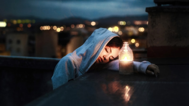 Girl in hoodie with candle on rooftop at night
