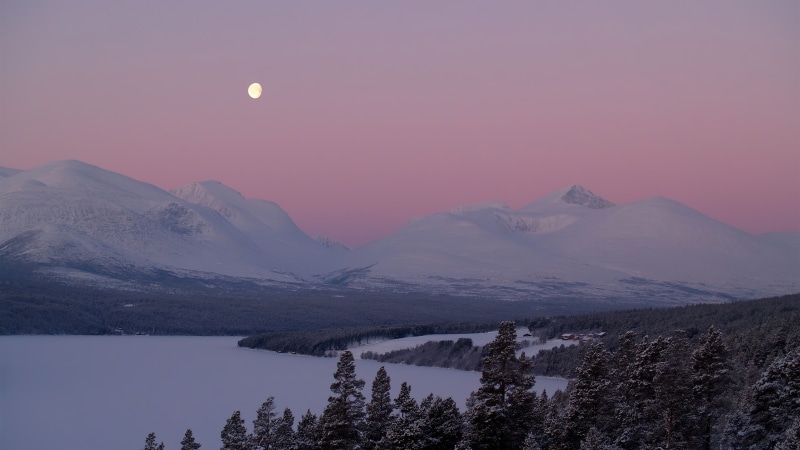 Moon over snow-covered mountains and frozen lake